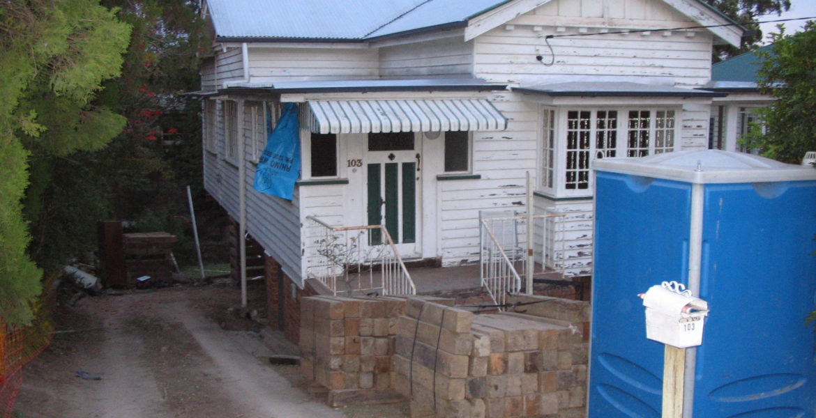 Old And Rundown Queenslander With Peeling White Paint And Untidy Exterior And Garden