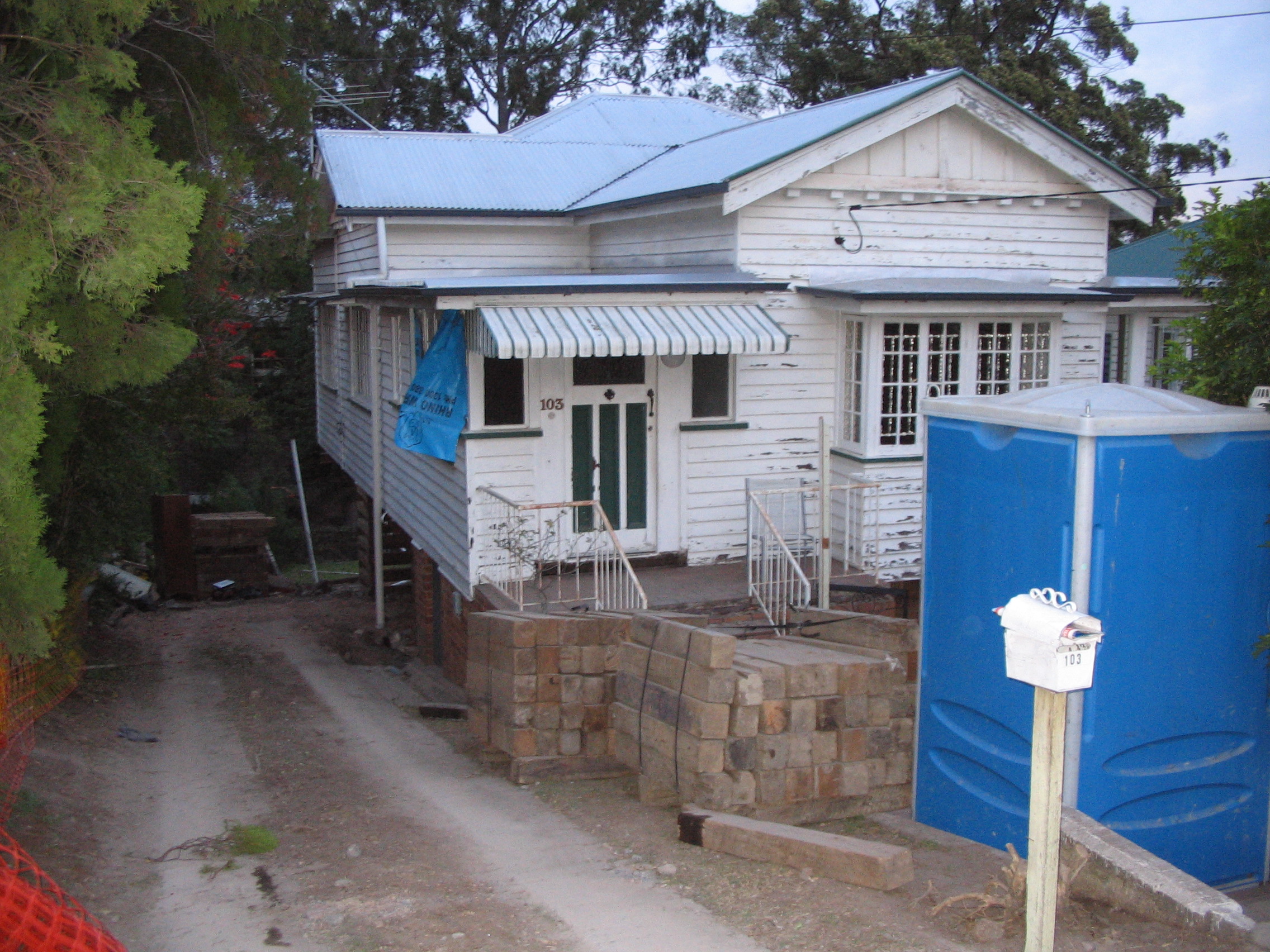 Old And Rundown Queenslander With Peeling White Paint And Untidy Exterior And Garden